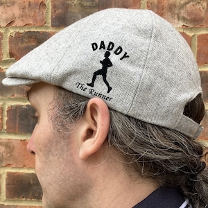 May include: A gray flat cap with a black silhouette of a running person and the text "Daddy The Runner" on the front.