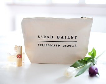 May include: A beige canvas makeup bag with a black zipper. The bag has the text "SARAH BAILEY" printed in black with a line underneath. Below the name, it says "BRIDESMAID 26.05.17" in black.