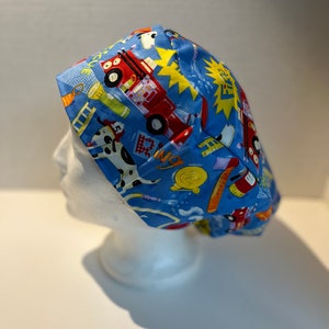 May include: Blue scrub hat with a fire truck and other firefighter themed illustrations. The hat has a tie on the back.