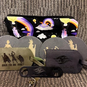 May include: A black zippered pouch with a colorful rainbow and character print, four round grey slate coasters with gold silhouettes, two rectangular luggage tags with character and logo prints, and a black metal bottle opener with a logo.