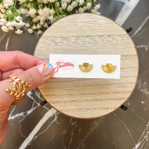 May include: A pair of gold fan-shaped earrings on a white card with the text "Pure Southern Designs".