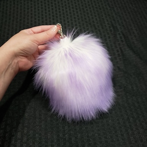 May include: A fluffy purple and white faux fur keychain with a silver metal clasp.