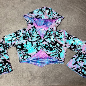 May include: A blue, black, and purple sequined crop top with a hood and long sleeves. The sleeves have a bell shape.
