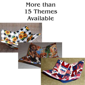 May include: Fabric bowl cozies in various themes. One features sunflowers on a black and white checkered background. Another has a dog theme, and a third has a patriotic theme with flags and stars. Text reads "More than 15 Themes Available."