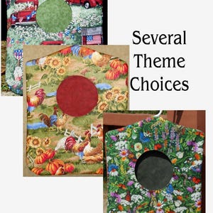 May include: Three fabric garment covers with central circular cutouts. One features red trucks and American flags on green, one shows roosters and sunflowers on green, and one displays colorful butterflies and wildflowers on a green background.