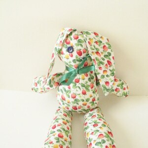 May include: A handmade stuffed bunny toy with a white fabric covered in a strawberry print. The bunny has green fabric ears and a green ribbon tied around its neck.