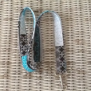 Puede incluir: Un cordón de color negro y blanco con un acento azul turquesa y un clip de metal plateado.