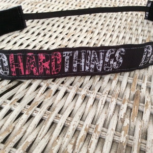 Puede incluir: Diadema negra con el texto "DO HARD THINGS" en letras blancas y rosas.
