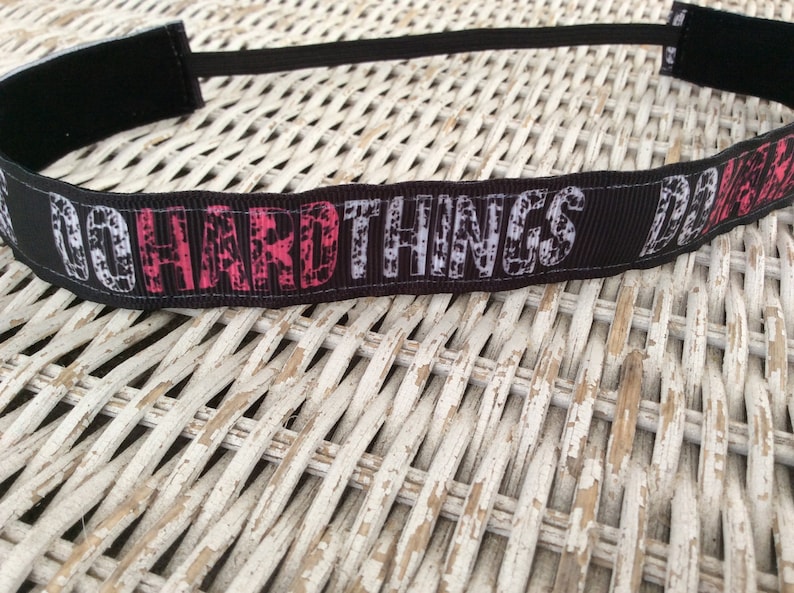 Puede incluir: Diadema negra con el texto "DO HARD THINGS" en letras blancas y rosas.