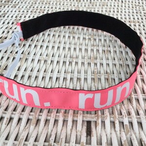 Puede incluir: Diadema rosa con banda el&aacute;stica negra y texto blanco que dice "run".
