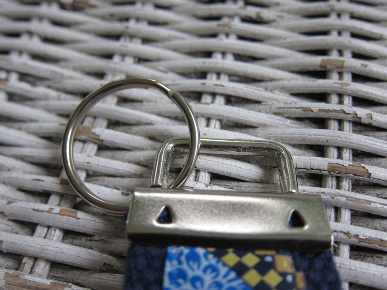 May include: A silver key ring with a ring and a metal clasp. The clasp is attached to a fabric strap with a blue, yellow and white patterned design.