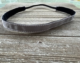 May include: A grey headband with a white dotted trim and black elastic. The headband is made of a soft, stretchy material.