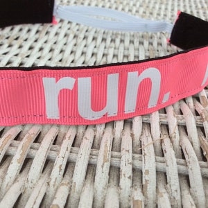 Puede incluir: Diadema rosa con el&aacute;stico blanco y la palabra "run." impresa en blanco en la parte delantera.