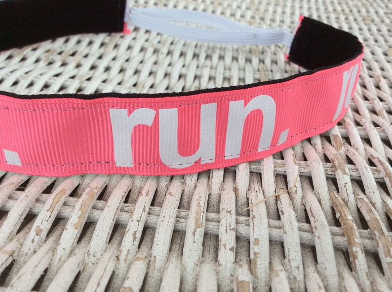 Puede incluir: Diadema rosa con el&aacute;stico blanco y la palabra "run." impresa en blanco en la parte delantera.