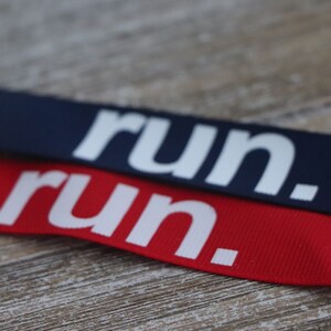 Puede incluir: Dos cintas de tela con la palabra "run." impresa en blanco sobre ellas. La cinta superior es azul marino y la cinta inferior es roja.