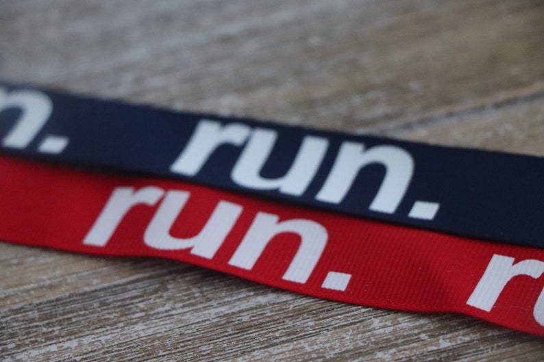 Puede incluir: Dos cintas de tela con la palabra "run." impresa en blanco sobre ellas. La cinta superior es azul marino y la cinta inferior es roja.