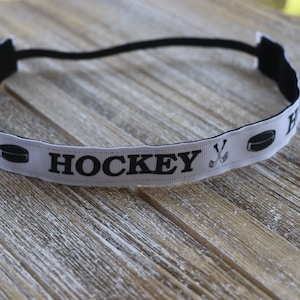 May include: White headband with black elastic and a white ribbon with the words "HOCKEY" and hockey stick and puck graphics.