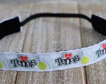 May include: White headband featuring the text "I Love Tennis" in black and red, with tennis ball and net graphics. The headband has a black elastic band, suitable for sports or athletic activities.