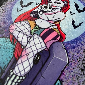 May include: A graphic illustration of a character with red hair, stitched skin, and a patchwork outfit, holding a small skull doll. The background features a full moon, bats, and a tombstone, creating a spooky, Halloween-themed design.