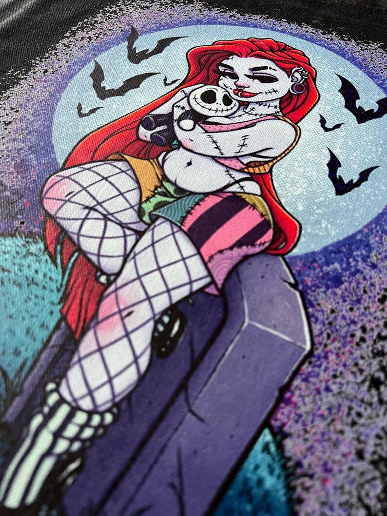 May include: A graphic illustration of a character with red hair, stitched skin, and a patchwork outfit, holding a small skull doll. The background features a full moon, bats, and a tombstone, creating a spooky, Halloween-themed design.