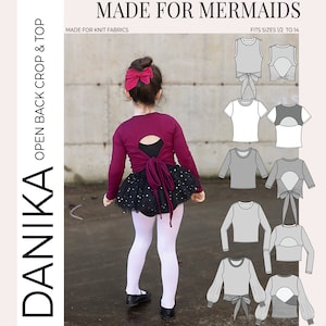 Puede incluir: Un patrón de costura para un top corto de espalda abierta para niñas con un lazo en la espalda. El patrón se llama "Danika" y está hecho para tejidos de punto. El patrón está disponible en tallas 1/2 a 14. El patrón se muestra en una modelo que lleva un top corto burdeos con una falda negra.