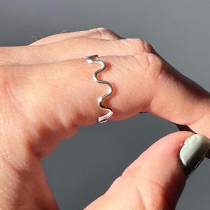May include: A silver ring with a wavy design. The ring is on a person's finger.