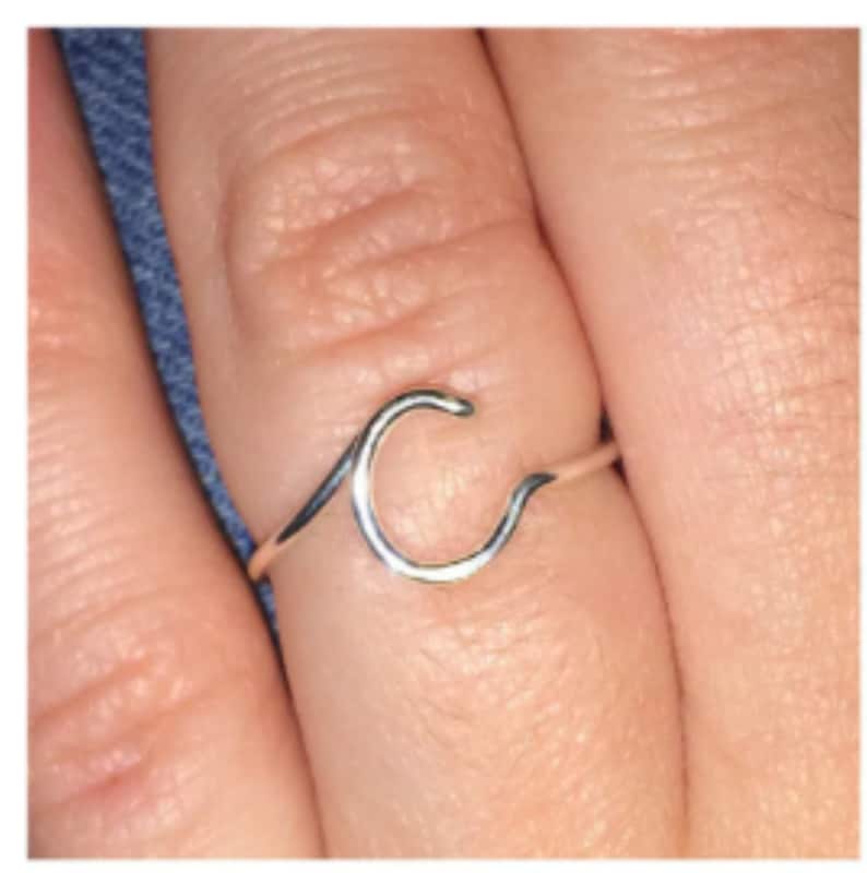 May include: A silver ring with a wave-shaped letter C design.