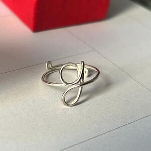 May include: A silver ring featuring a cursive letter G design.