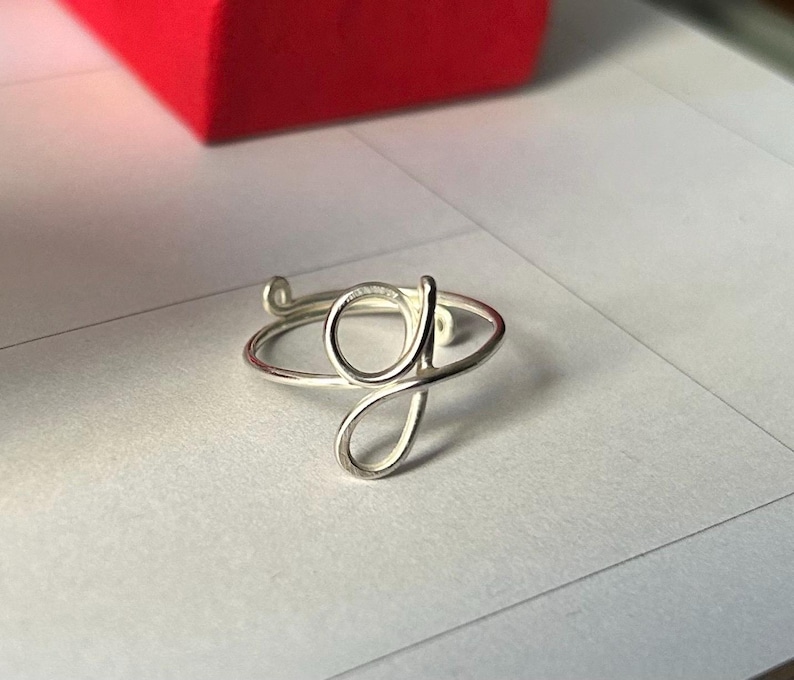 May include: A silver ring featuring a cursive letter G design.