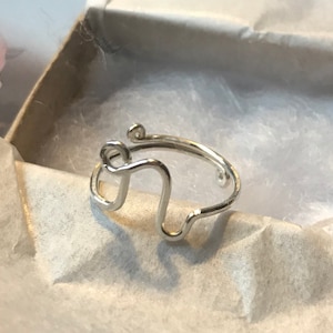 May include: A silver ring featuring a distinctive, abstract design. The ring is crafted from thin wire and has a simple, minimalist style.
