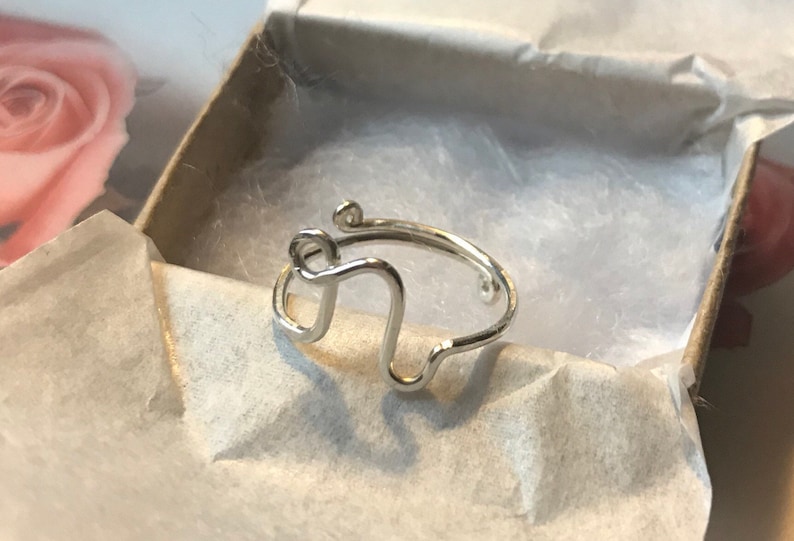 May include: A silver ring featuring a distinctive, abstract design. The ring is crafted from thin wire and has a simple, minimalist style.