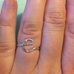 May include: A silver ring featuring a simple, wavy 'e' design.