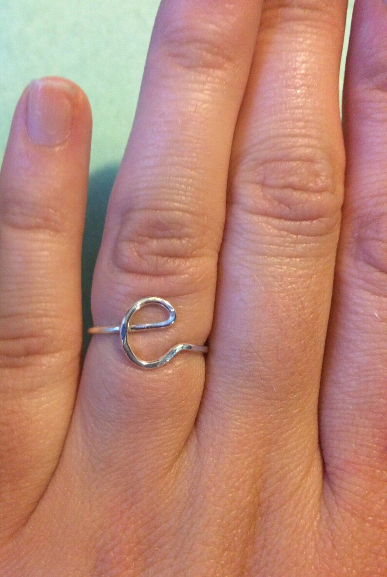 May include: A silver ring featuring a simple, wavy 'e' design.