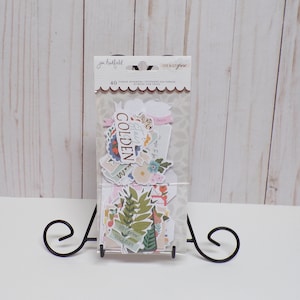 May include: A package of 40 phrase stickers with a floral and botanical theme. The stickers feature phrases like "Stay Golden", "We Grow Together", and "Hello", and are printed on white paper with a pink and green color scheme.