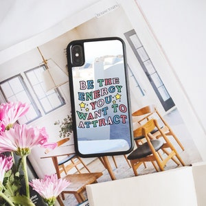 May include: A black phone case with a clear back and a colourful quote that reads "Be the energy you want to attract". The quote is in a retro font with stars.