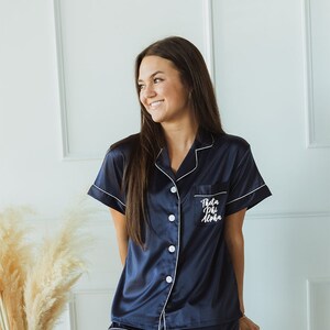 Puede incluir: Un conjunto de pijama de satén azul marino con ribetes blancos y un bolsillo en el lado izquierdo de la camisa que dice "Theta Phi Alpha" en escritura blanca.