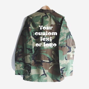 Puede incluir: Una chaqueta de camuflaje verde y marr&oacute;n con un texto blanco superpuesto que dice "Your custom text or logo".
