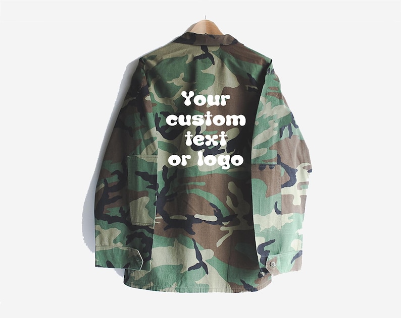 Puede incluir: Una chaqueta de camuflaje verde y marr&oacute;n con un texto blanco superpuesto que dice "Your custom text or logo".