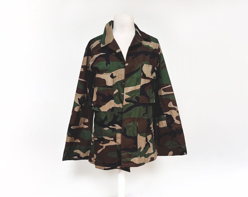 Puede incluir: Una chaqueta de camuflaje con cierre de botones y varios bolsillos.