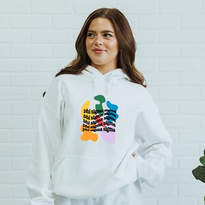 May include: White hoodie with a colourful abstract design featuring the text "Phi Sigma Sigma" repeated multiple times.