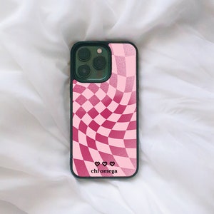 Può includere: Una custodia per telefono a scacchi rosa e rossa con bordo nero e il testo "chi omega" e tre cuori.