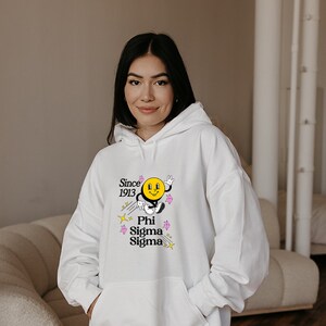 May include: White hooded sweatshirt with a yellow smiley face graphic and the text "Since 1913 Phi Sigma Sigma" in black.