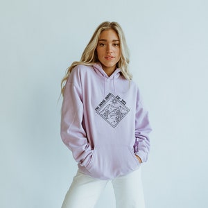 May include: A lavender hoodie with a black diamond-shaped graphic featuring a mountain range, a sun, and cacti. The graphic also includes the text "Phi Sigma Sigma Est. 1912".