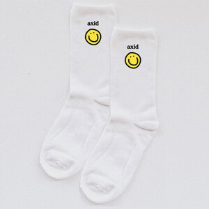 May include: A pair of white socks with a yellow smiley face and the word "axid" printed on each sock.