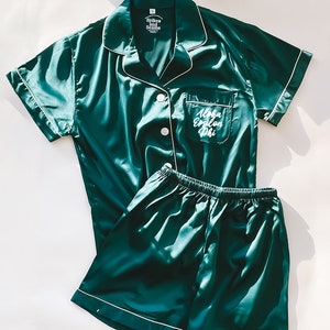 Puede incluir: Un conjunto de pijama de satén verde con mangas cortas y pantalones cortos. La parte superior tiene un bolsillo blanco con el texto "Alpha Epsilon Phi" bordado. El conjunto tiene ribetes blancos alrededor de los bordes.