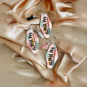 May include: Two pink and green keychains with the text "ALPHA PHI ESTABLISHED 1872" on a light brown satin background.