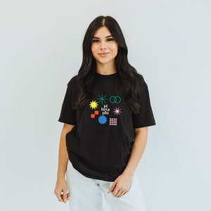 Puede incluir: Una camiseta negra con un diseño gráfico colorido que presenta formas geométricas y el texto "pi beta phi".