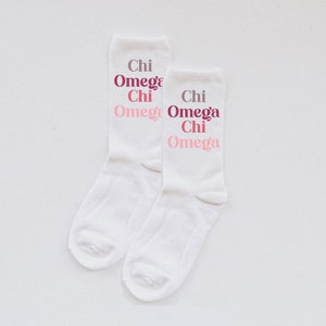 May include: A pair of white socks with the text "Chi Omega Chi Omega" printed in pink and burgundy.