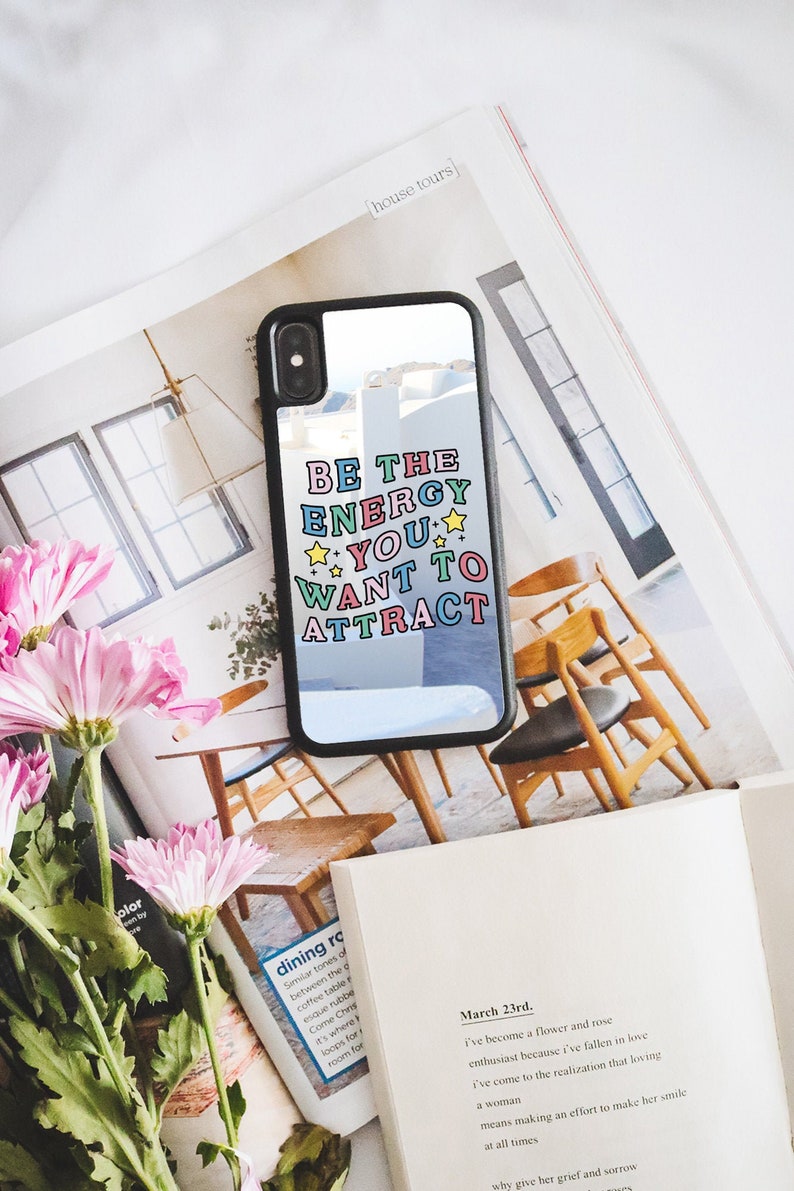 May include: A black phone case with a clear back and a colourful quote that reads "Be the energy you want to attract". The quote is in a retro font with stars.