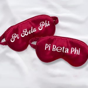 Puede incluir: Dos antifaces de satén rojo con texto bordado en blanco que dice "Pi Beta Phi".